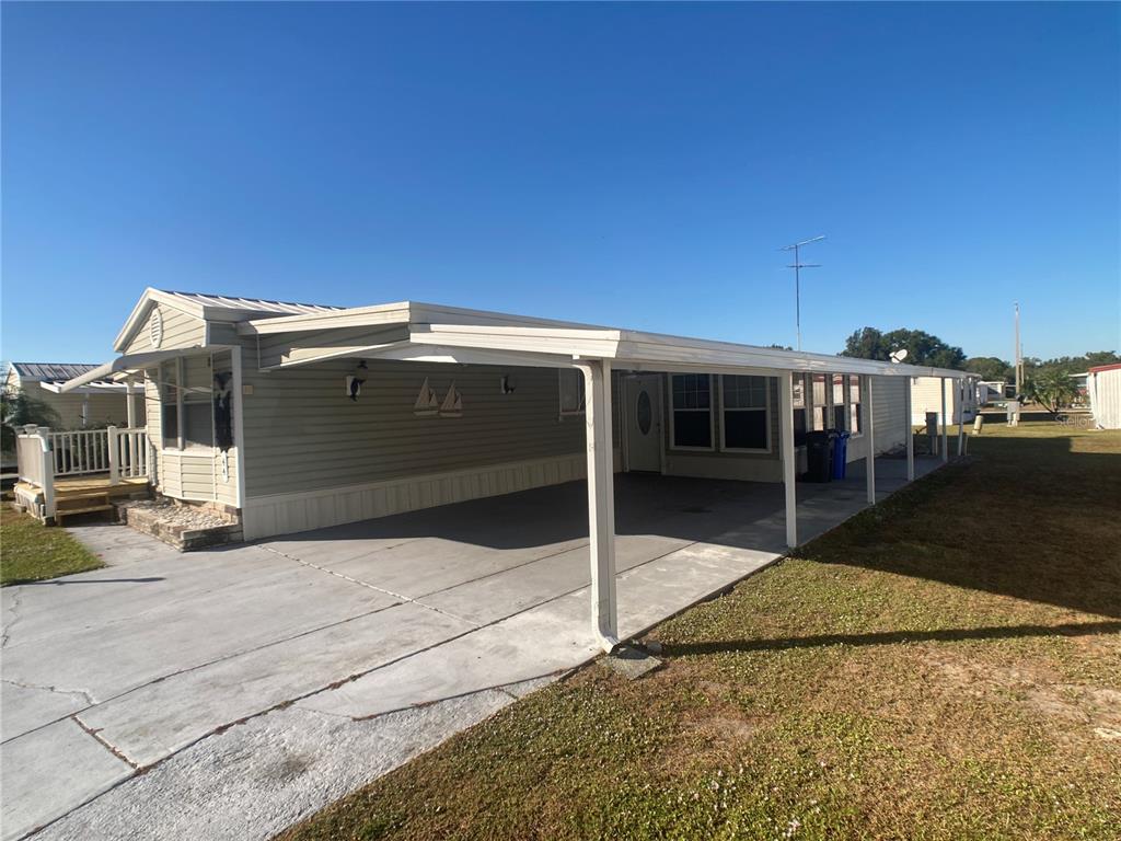 A single-story manufactured home features a large attached carport and a small front deck — 1710 7TH STREET SW UNIT 44, RUSKIN, FL