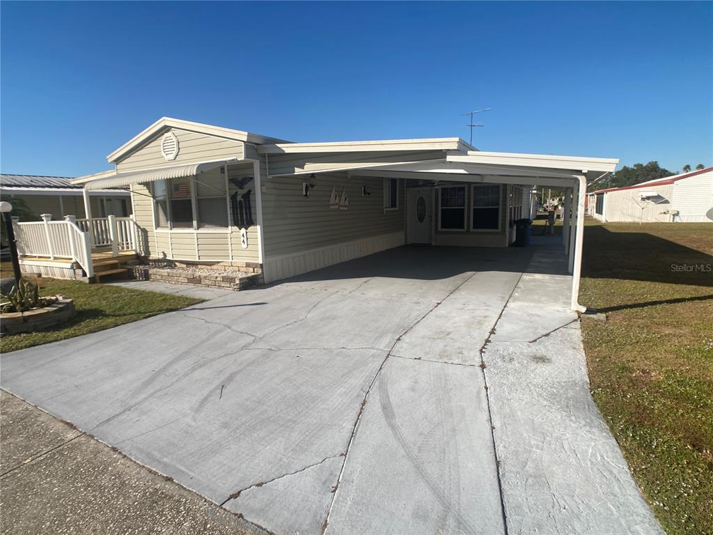 A single-story manufactured home features light siding, a concrete driveway, and an attached carport — 1710 7TH STREET SW UNIT 44, RUSKIN, FL
