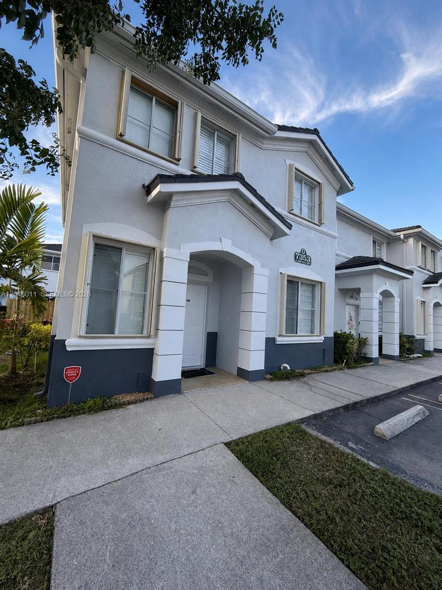 A two-story townhouse exterior with a white facade, dark gray base, and a covered entryway — 7353 NW 174th Ter # 107, Hialeah FL 33015, HIALEAH, FL