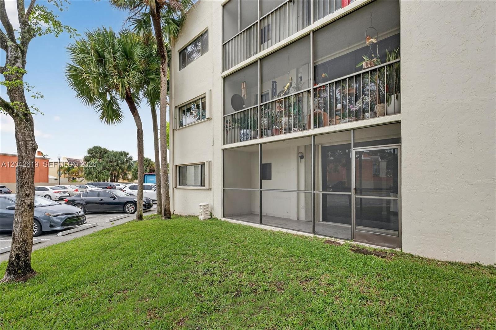 The exterior of a multi-story apartment building features screened-in balconies and a grassy lawn — 8065 SW 107th Ave # 106, Miami FL 33173, MIAMI, FL