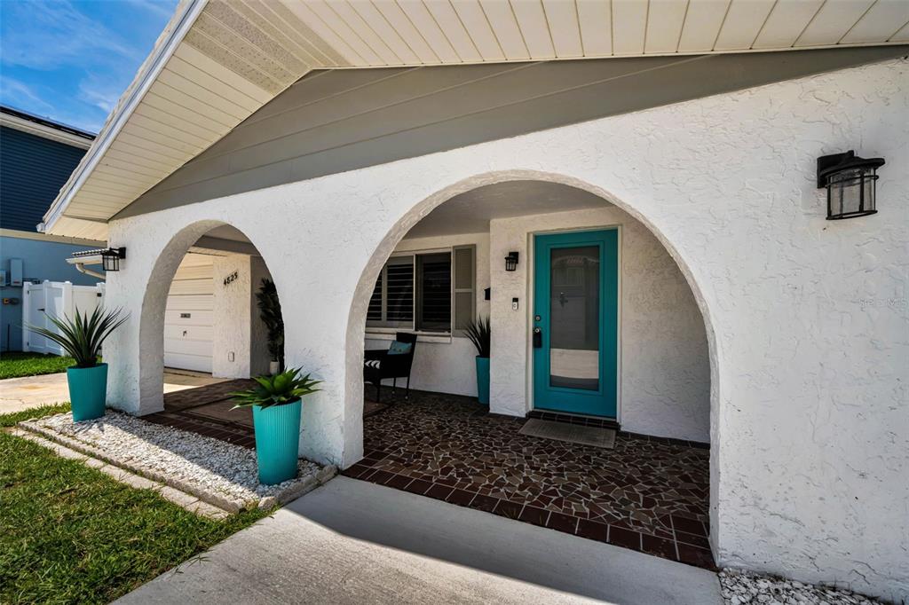 A white house exterior features two arched entryways, a teal front door, and potted plants — 4825 SHELL STREAM BOULEVARD, NEW PORT RICHEY, FL
