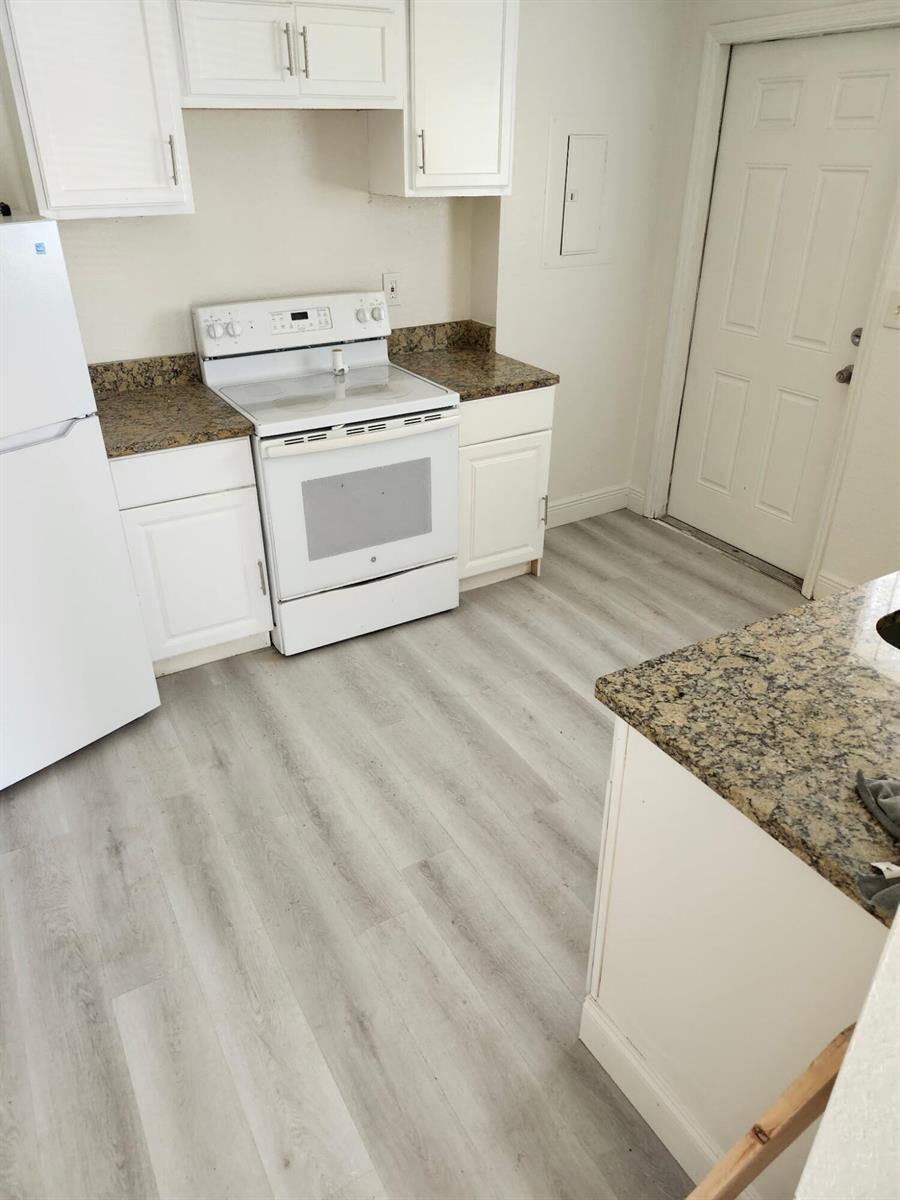 A kitchen features white cabinets, granite countertops, a white stove, and light wood-look flooring — 1401 G Terrace, Fort Pierce FL 34950, FORT PIERCE, FL