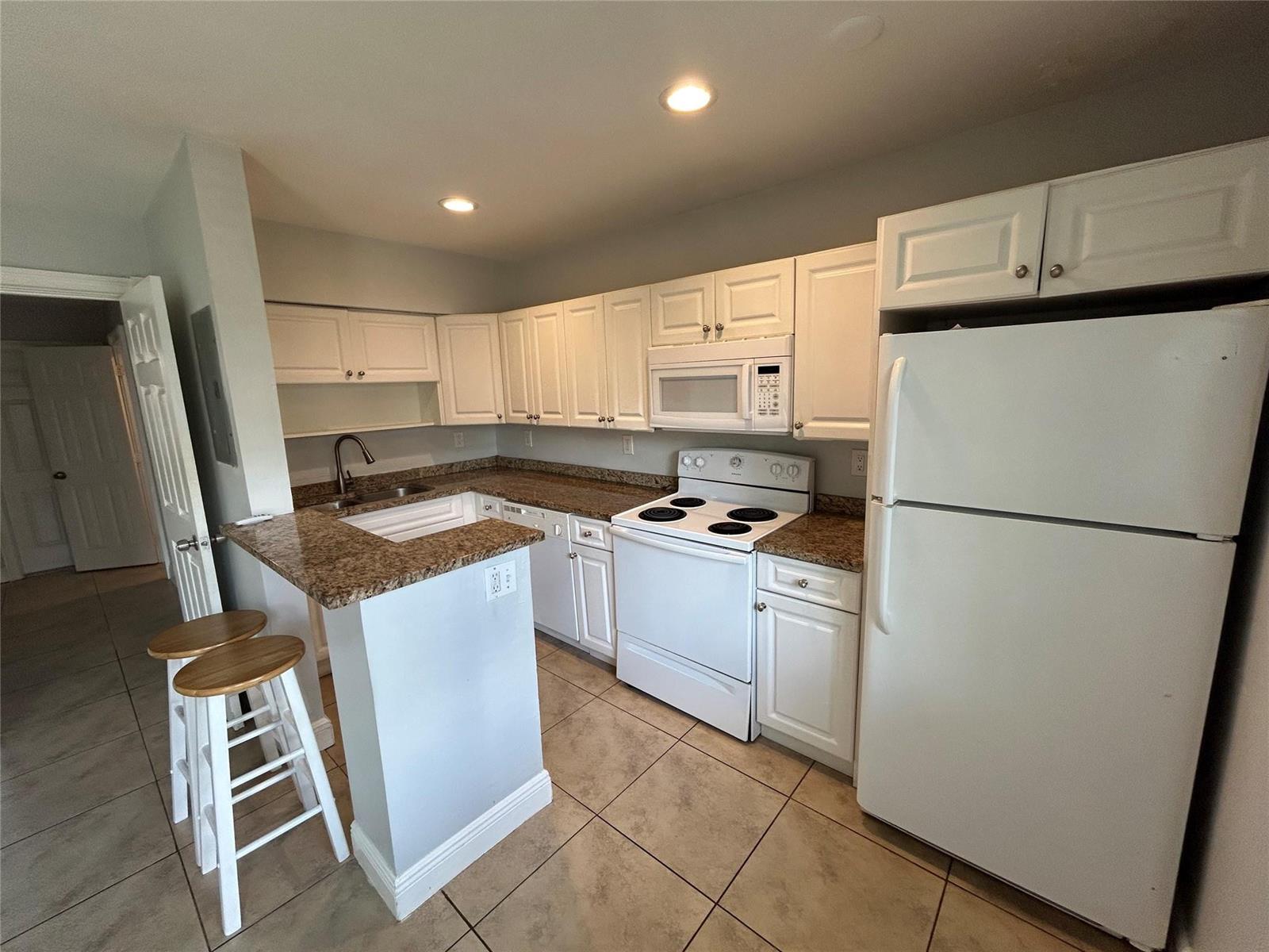 A kitchen features white cabinets, granite countertops, white appliances, and a breakfast bar with stools — 921 NE 17th Avenue # 2, Fort Lauderdale FL 33304, FORT LAUDERDALE, FL
