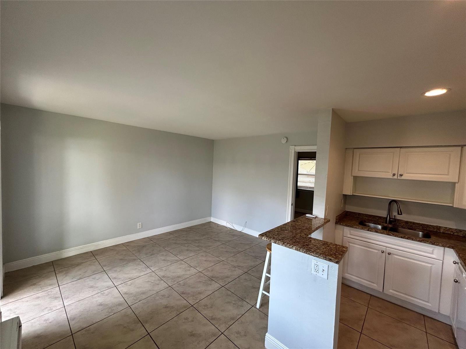 An open-concept kitchen with granite countertops and tile flooring flows into a living area — 921 NE 17th Avenue # 2, Fort Lauderdale FL 33304, FORT LAUDERDALE, FL