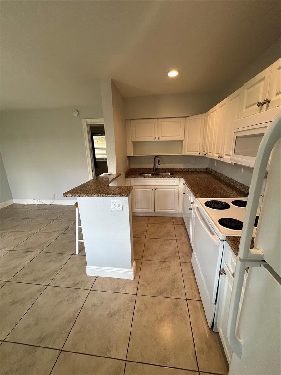 A kitchen features white cabinets, granite countertops, tile flooring, and a breakfast bar — 921 NE 17th Avenue # 2, Fort Lauderdale FL 33304, FORT LAUDERDALE, FL