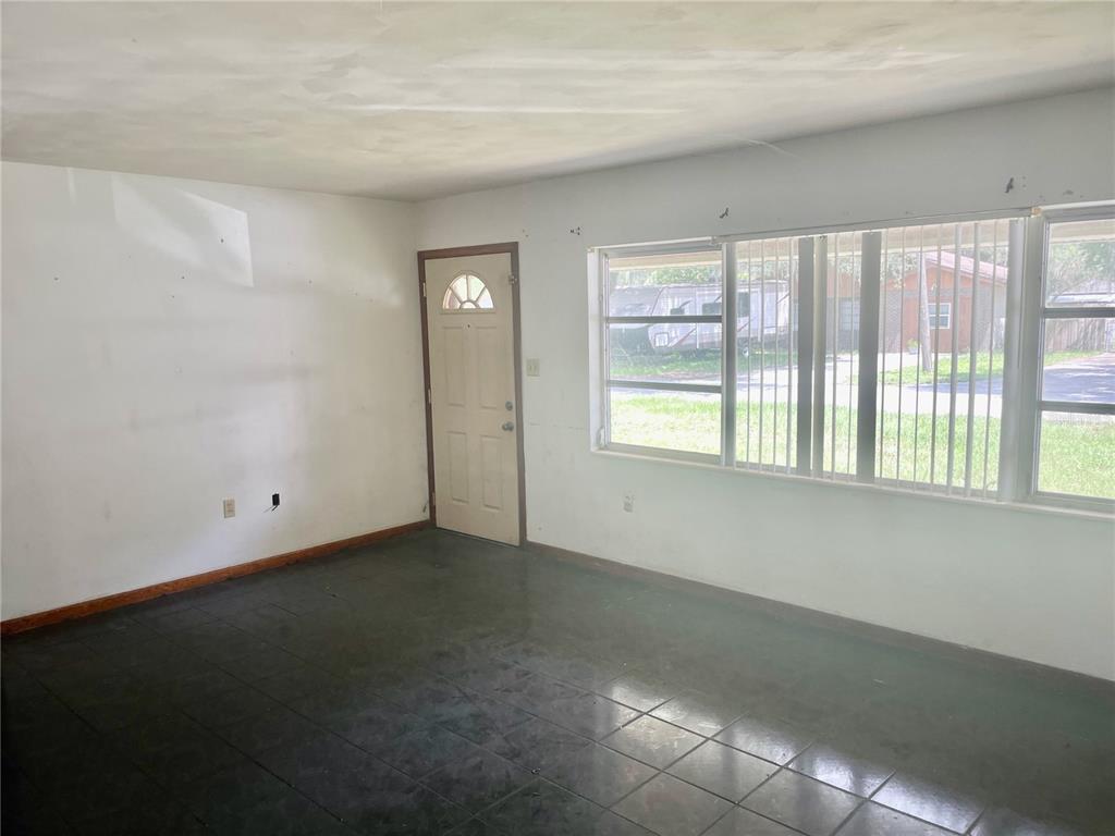 An empty room with dark tile flooring, white walls, a front door, and large windows — 2033 VOLTAIRE STREET, LAKELAND, FL