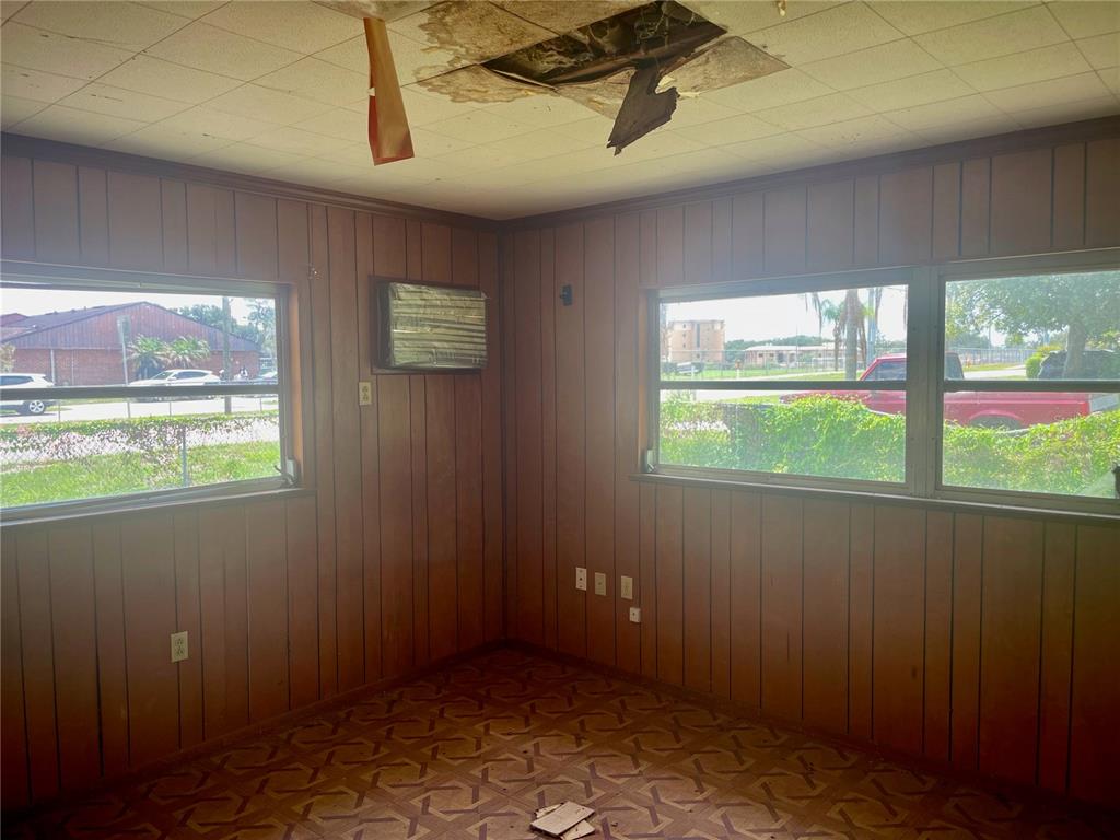 A room with wood-paneled walls, patterned flooring, and a damaged ceiling with exposed material — 2033 VOLTAIRE STREET, LAKELAND, FL