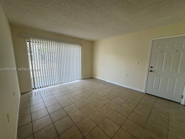 An empty room features beige tile flooring, a sliding glass door with blinds, and a door — 7030 NW 179th St # 104, Hialeah FL 33015, HIALEAH, FL
