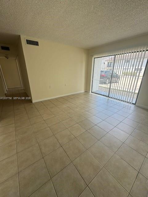 An empty living room with beige tile flooring, light walls, and a sliding glass door — 7030 NW 179th St # 104, Hialeah FL 33015, HIALEAH, FL