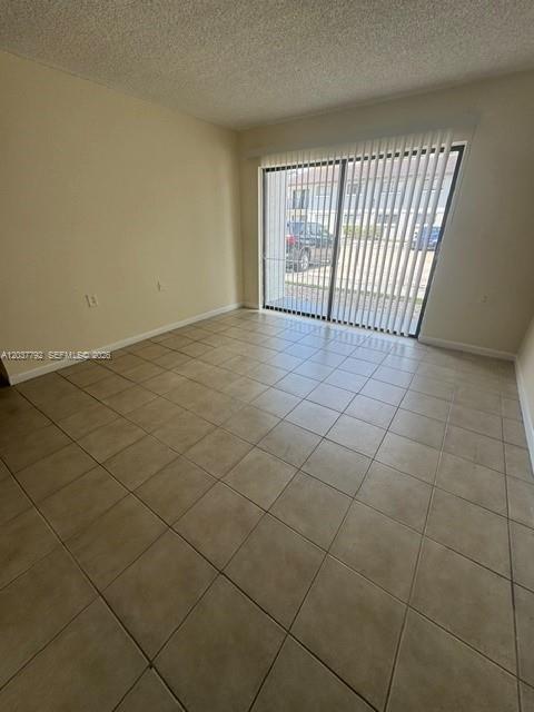 An empty room with beige tile flooring and a sliding glass door leading outside — 7030 NW 179th St # 104, Hialeah FL 33015, HIALEAH, FL