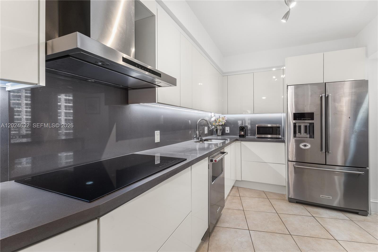 A modern kitchen features white glossy cabinets, stainless steel appliances, and a dark gray backsplash — 20281 E Country Club Dr # 510, Aventura FL 33180, AVENTURA, FL