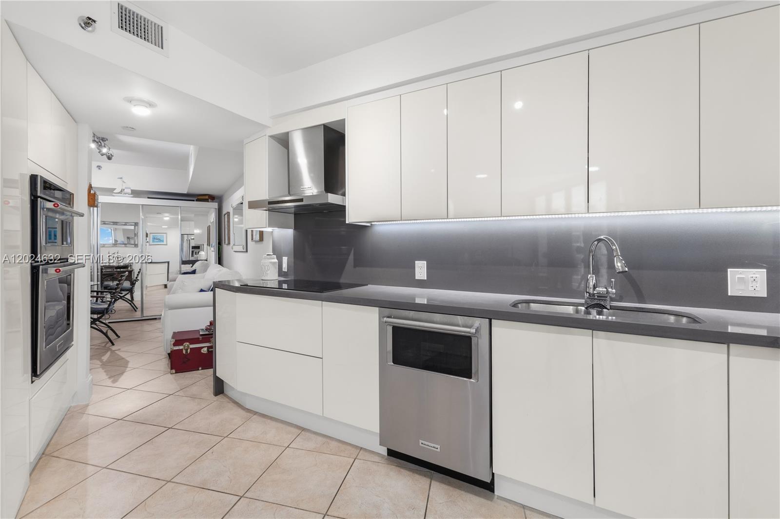 A modern kitchen features white glossy cabinets, dark gray countertops, and stainless steel appliances — 20281 E Country Club Dr # 510, Aventura FL 33180, AVENTURA, FL