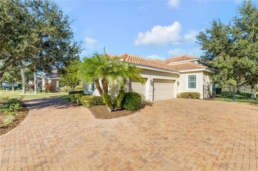 A tan house with a tiled roof and a brick paver driveway sits among trees — 3021 ISOLA BELLA BOULEVARD, MOUNT DORA, FL