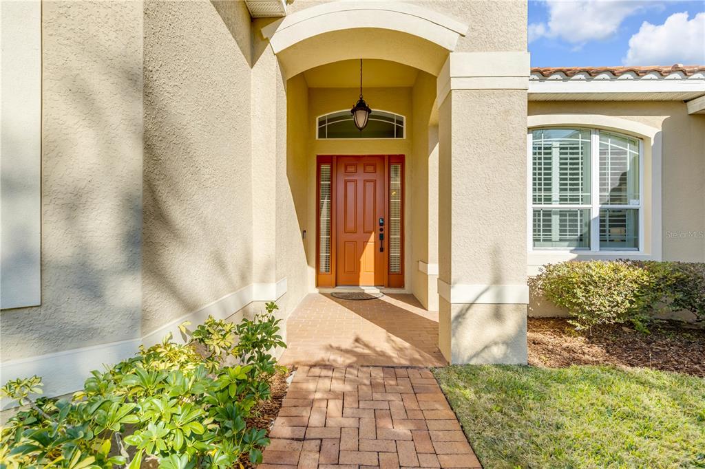 A brick walkway leads to a recessed front entrance with a wooden door and sidelights — 3021 ISOLA BELLA BOULEVARD, MOUNT DORA, FL