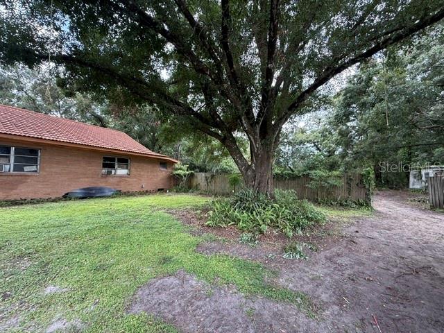 A brick house with a tile roof stands next to a large tree and yard — 3011 S WIGGINS ROAD, PLANT CITY, FL