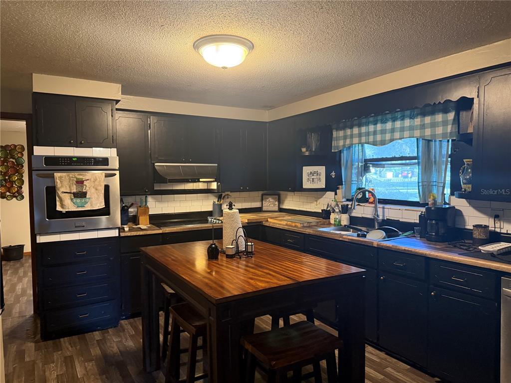 A kitchen features black cabinets, a wooden island, stainless steel appliances, and a tiled backsplash — 3011 S WIGGINS ROAD, PLANT CITY, FL