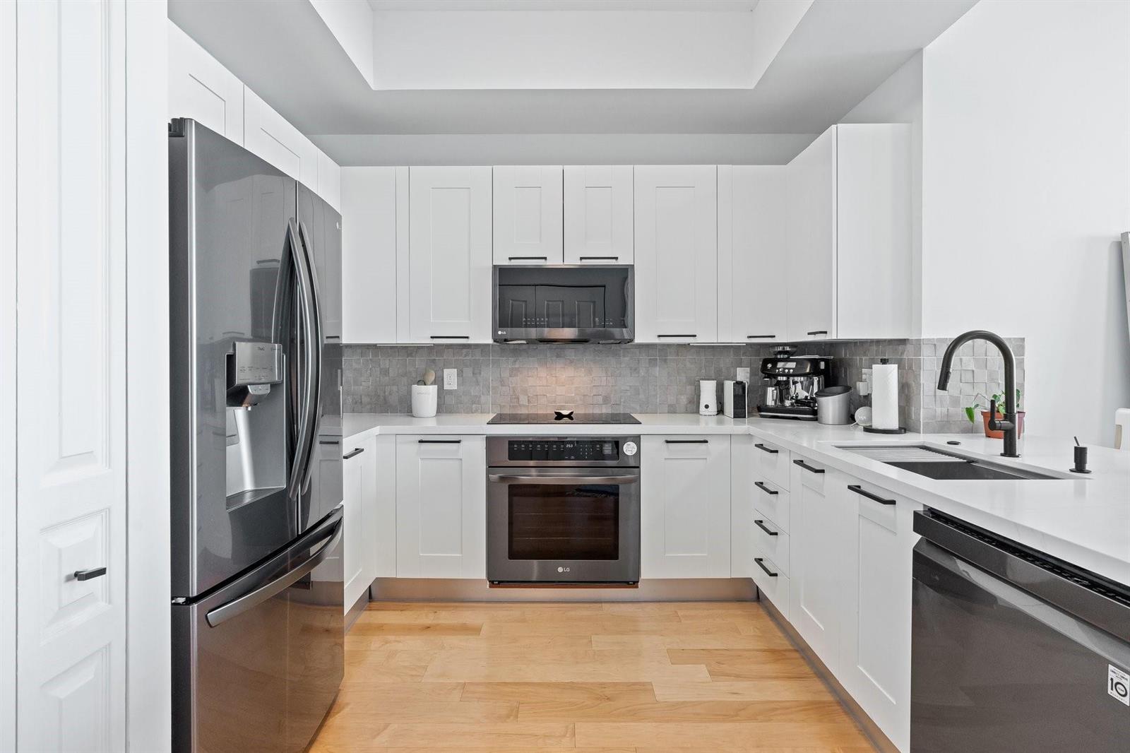 A modern kitchen features white cabinetry, stainless steel appliances, a gray tile backsplash, and wood flooring — 350 SE 2nd Street # 2960, Fort Lauderdale FL 33301, FORT LAUDERDALE, FL