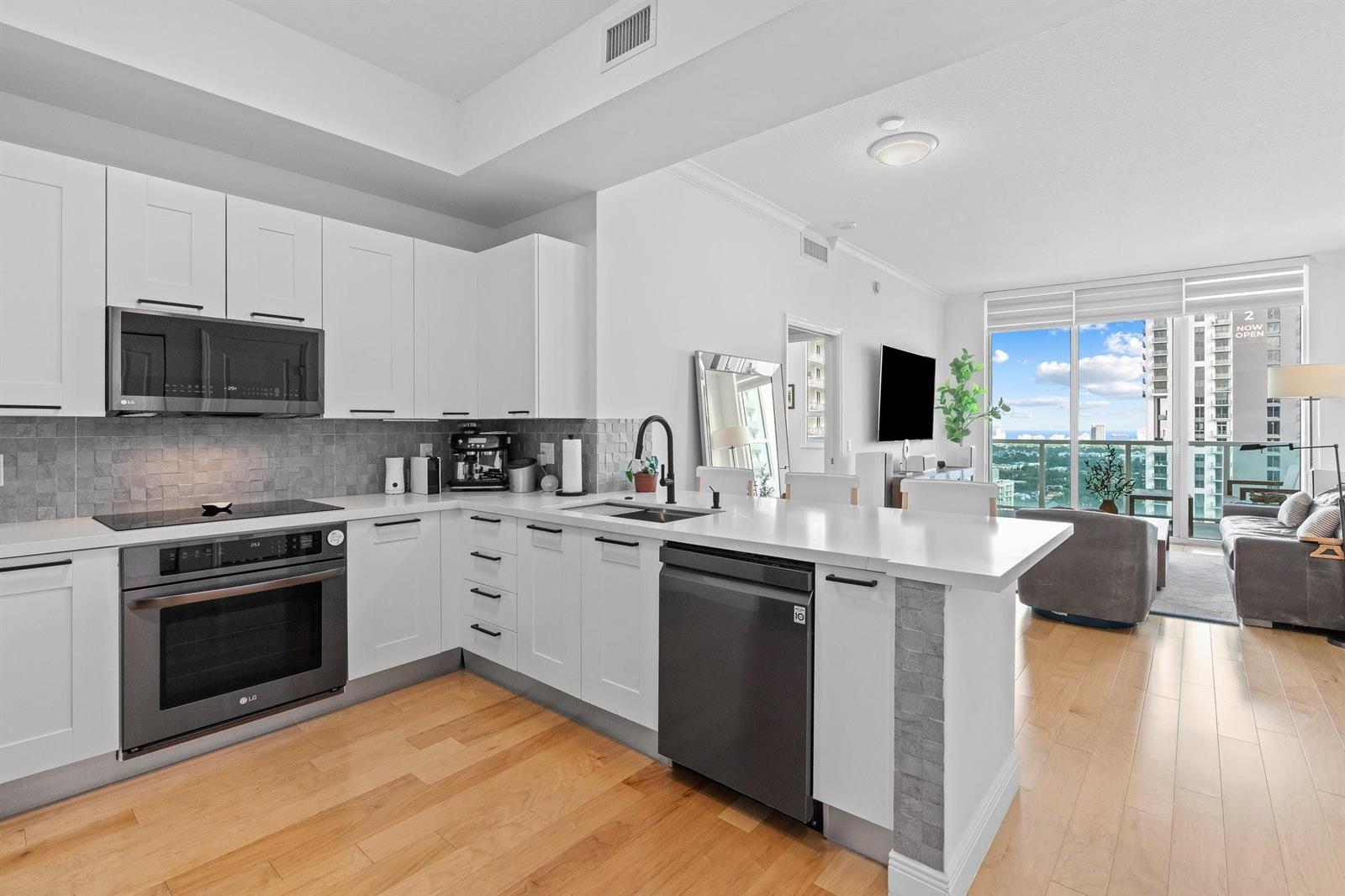 A modern kitchen with white cabinets, stainless steel appliances, and wood flooring opens to a living area — 350 SE 2nd Street # 2960, Fort Lauderdale FL 33301, FORT LAUDERDALE, FL
