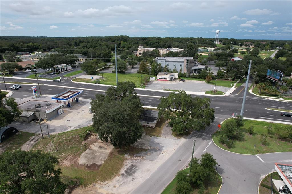 An aerial view shows a vacant lot with trees next to a gas station and road — 138 W HERMOSA STREET, LADY LAKE, FL