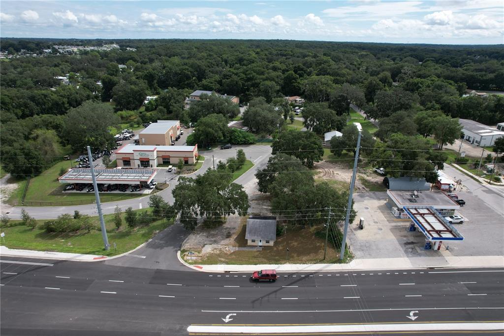 An aerial view shows a commercial property with a small building, parking, and a gas station — 138 W HERMOSA STREET, LADY LAKE, FL