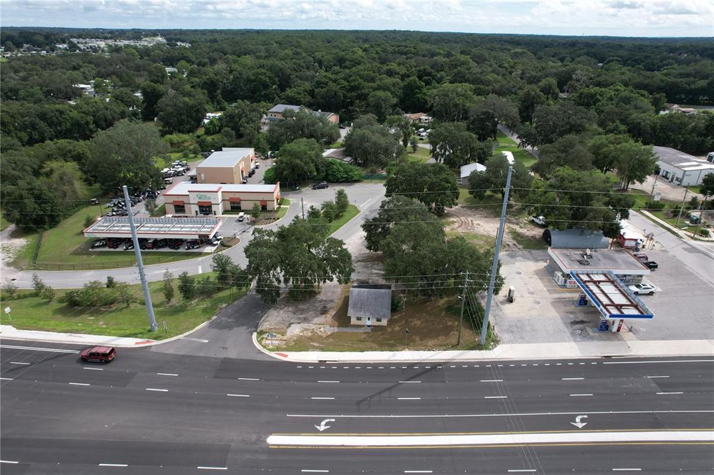 An aerial view shows a small house situated between a commercial dealership and a gas station — 138 W HERMOSA STREET, LADY LAKE, FL