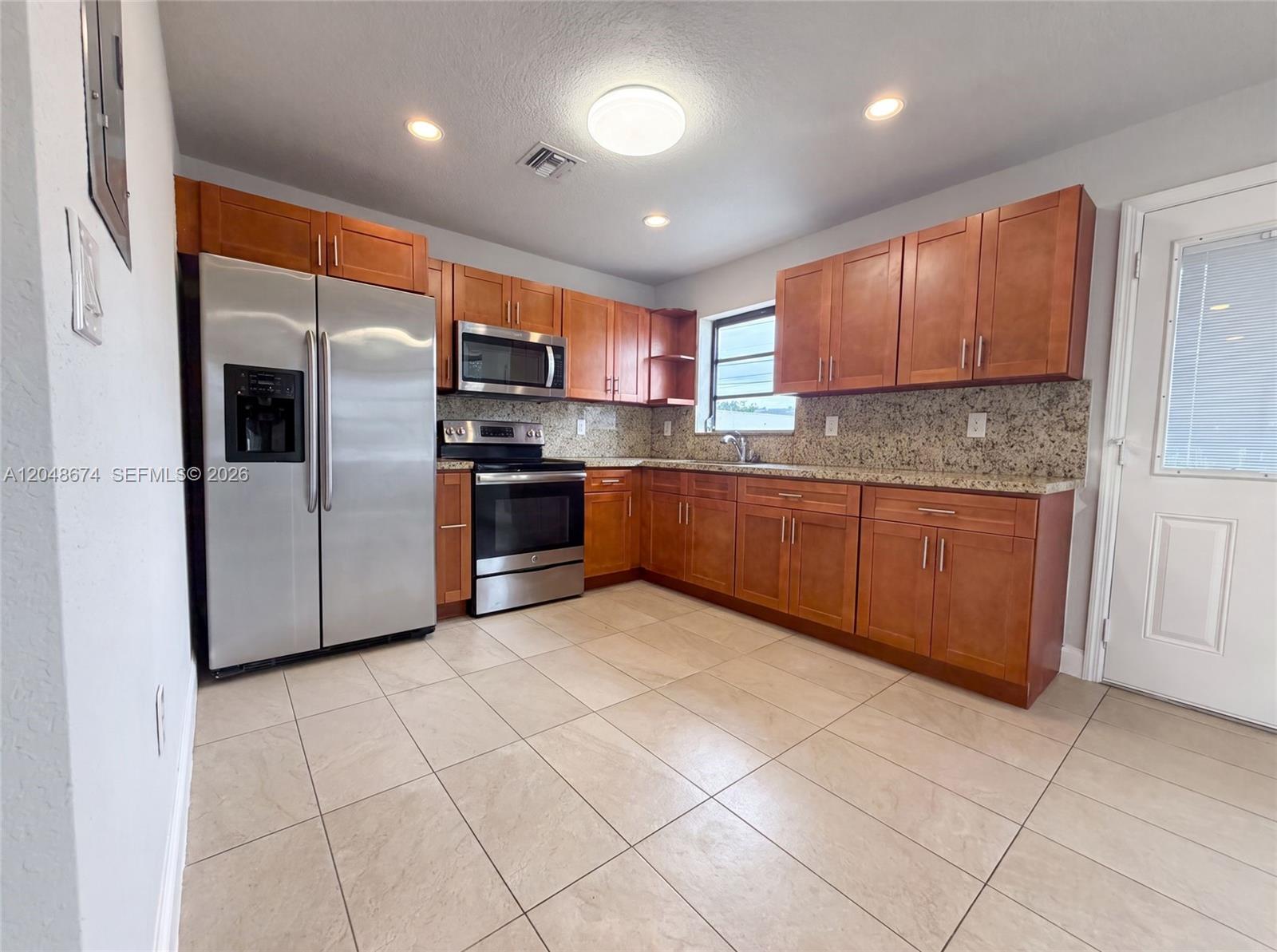 A kitchen features wooden cabinets, granite countertops, stainless steel appliances, and beige tile flooring — 8340 NW 22nd Pl, Miami FL 33147, MIAMI, FL