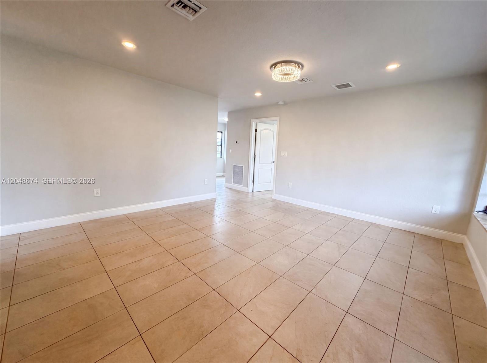 A spacious room features light-colored walls, tan tile flooring, and a central crystal light fixture — 8340 NW 22nd Pl, Miami FL 33147, MIAMI, FL