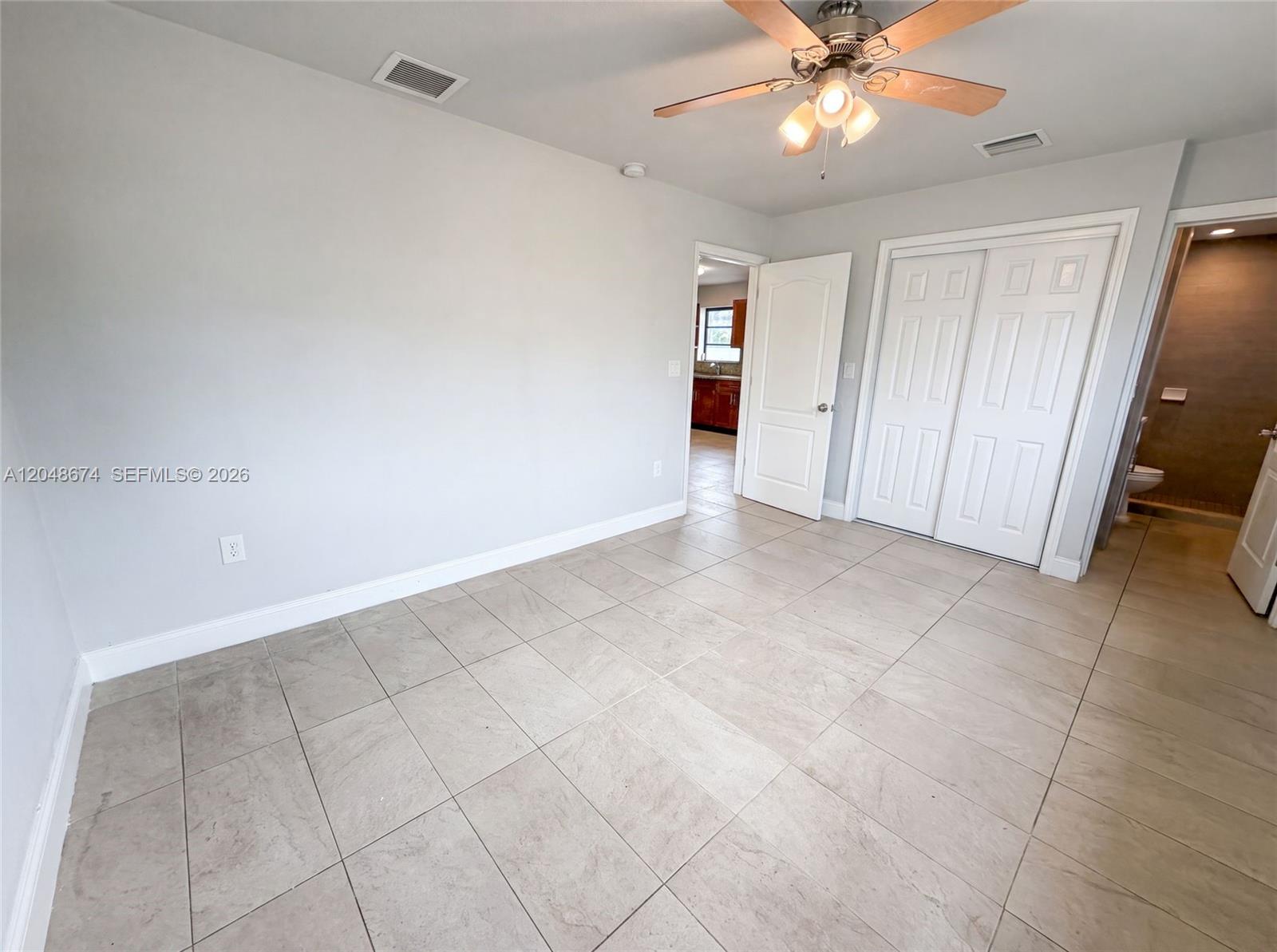 A bedroom with light gray walls, tile flooring, a ceiling fan, and an attached bathroom — 8340 NW 22nd Pl, Miami FL 33147, MIAMI, FL