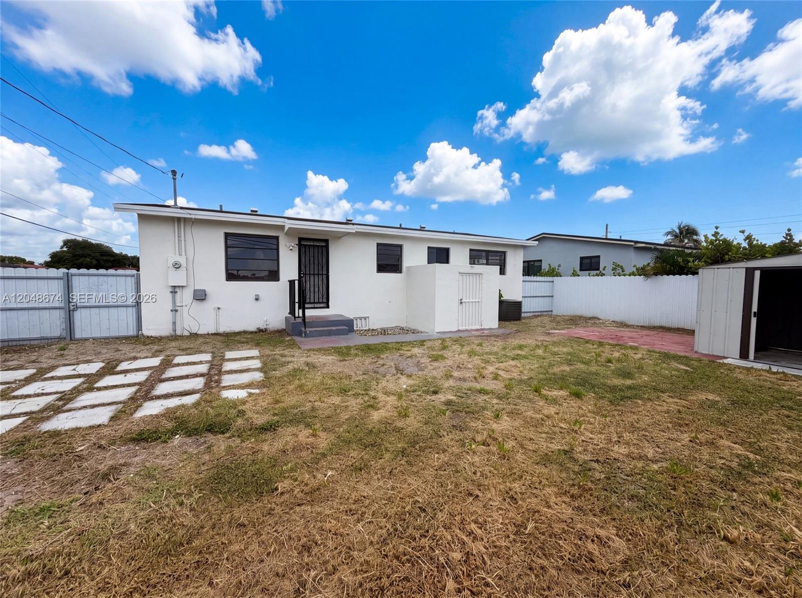 The exterior of a white house features a backyard with a shed and paved walkway — 8340 NW 22nd Pl, Miami FL 33147, MIAMI, FL