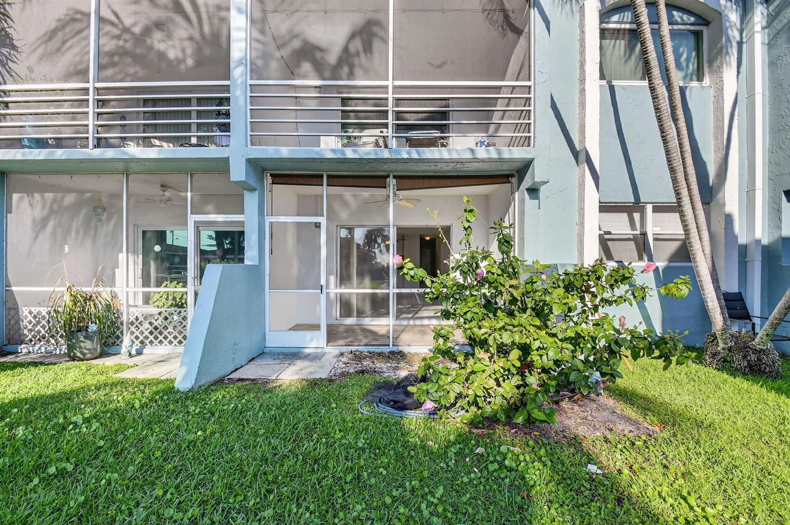 The exterior of a multi-story building features screened-in patios, a small garden, and palm trees — 1432 S Lakeside Drive # 4, FL 33460, FL