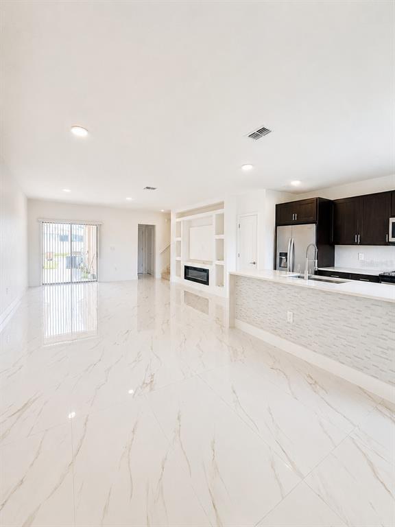 An open-concept living area features white marble-look tile flooring, a fireplace, and a modern kitchen — 1562 CARBONDALE ROW, KISSIMMEE, FL