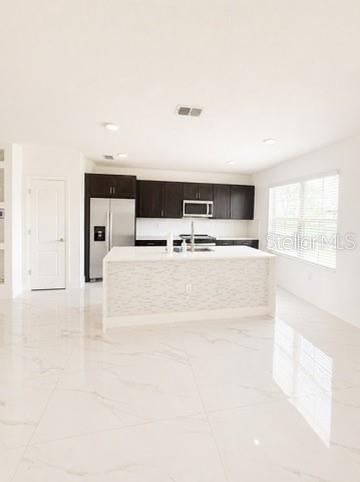A modern kitchen features dark cabinets, a white island, and light-colored marble-look tile flooring — 1562 CARBONDALE ROW, KISSIMMEE, FL