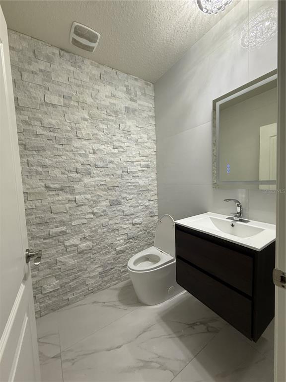 A modern powder room featuring a textured stone accent wall, marble-look flooring, and a floating vanity — 1562 CARBONDALE ROW, KISSIMMEE, FL