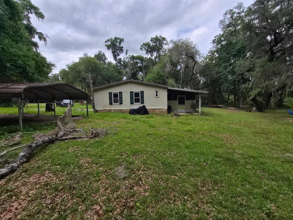 A single-story house with light siding and a metal carport sits on a grassy lot — 14179 NE 53RD COURT ROAD, CITRA, FL