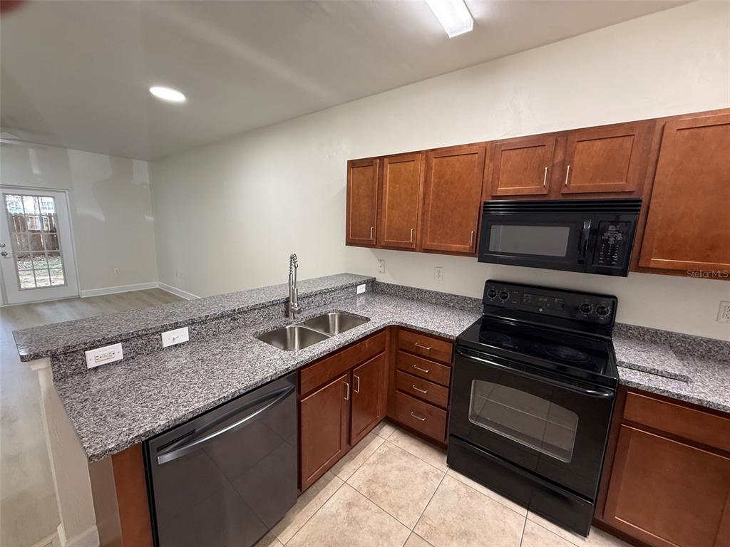 A kitchen features granite countertops, dark wood cabinets, black appliances, and tile flooring — 2945 SW 35TH PLACE UNIT 132, GAINESVILLE, FL