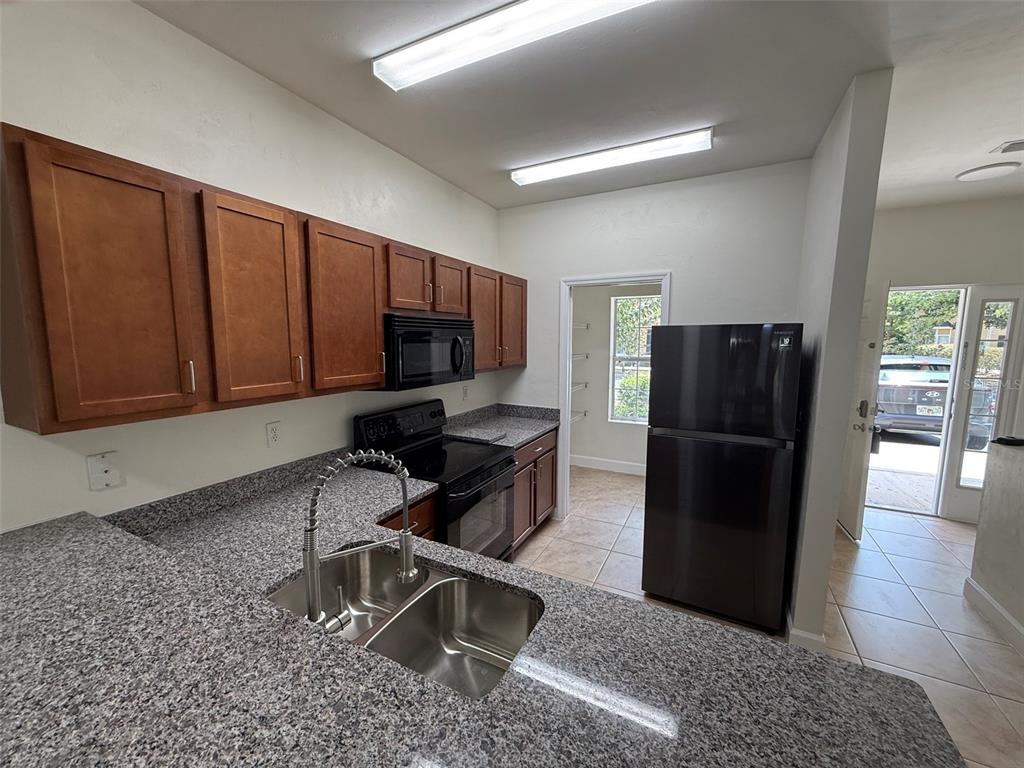 A kitchen features granite countertops, wood cabinets, black appliances, and a view of an exterior doorway — 2945 SW 35TH PLACE UNIT 132, GAINESVILLE, FL