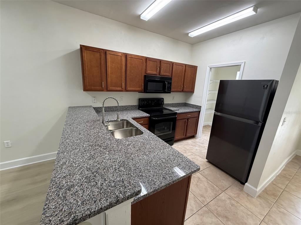 A kitchen features granite countertops, wood cabinets, black appliances, and a tile floor — 2945 SW 35TH PLACE UNIT 132, GAINESVILLE, FL