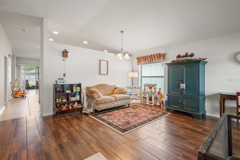 A living room with wood-look tile flooring, a tan sofa, and a large teal cabinet — 15585 LILY WOOD LANE, BROOKSVILLE, FL