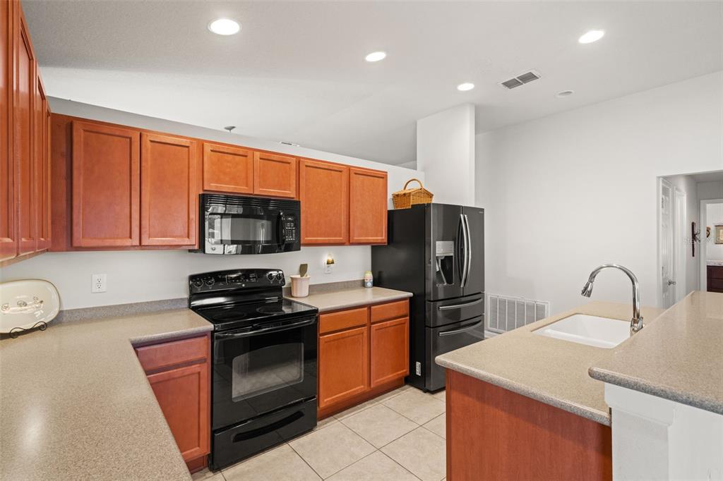 A kitchen features wood cabinets, black appliances, tan countertops, and a central island with sink — 15585 LILY WOOD LANE, BROOKSVILLE, FL