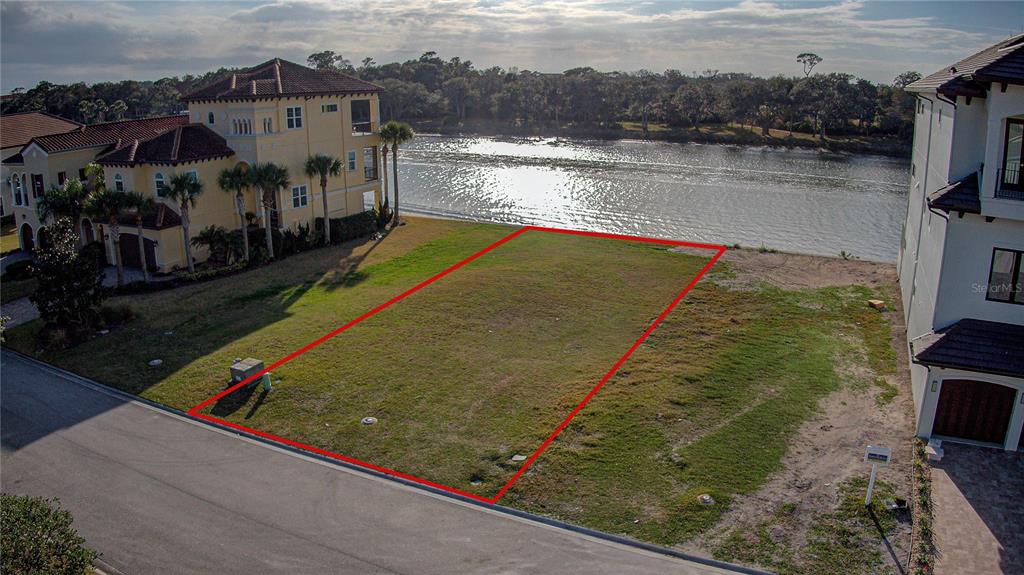 An aerial view shows a vacant, rectangular waterfront lot outlined in red between two houses — 276 YACHT HARBOR DRIVE, PALM COAST, FL