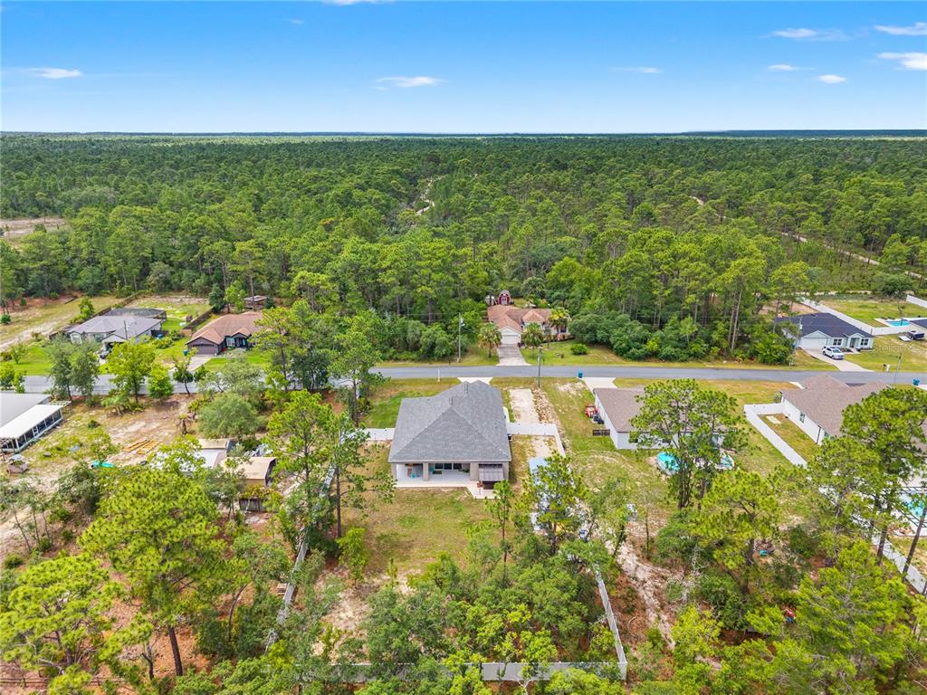 An aerial view shows a single-story house with a gray roof surrounded by wooded lots — 11153 WOOD OWL AVENUE, WEEKI WACHEE, FL