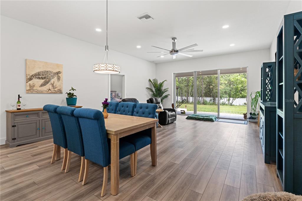 A dining area with blue upholstered chairs and a wooden table opens to a backyard — 11153 WOOD OWL AVENUE, WEEKI WACHEE, FL