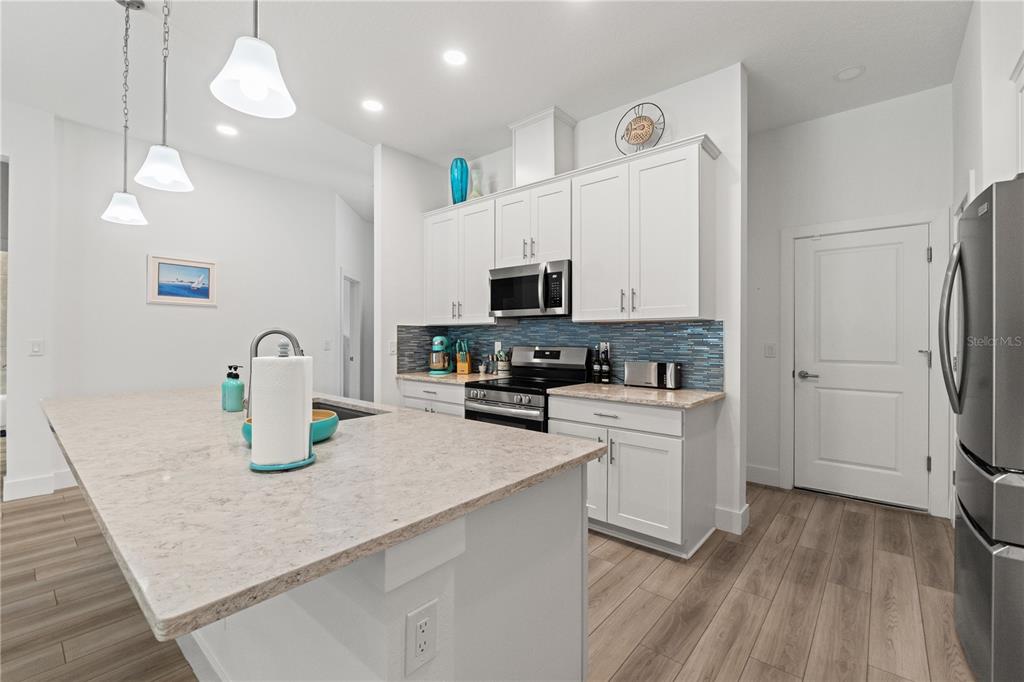 A modern kitchen features white cabinets, a granite island, and a blue tile backsplash — 11153 WOOD OWL AVENUE, WEEKI WACHEE, FL