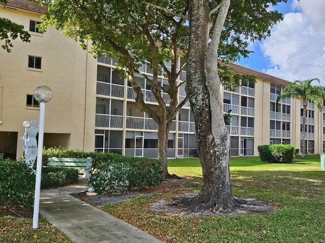 A multi-story apartment building with screened balconies, a large tree, and a statue in front — 300 Village Green Circle S # 209, Palm Springs FL 33461, PALM SPRINGS, FL