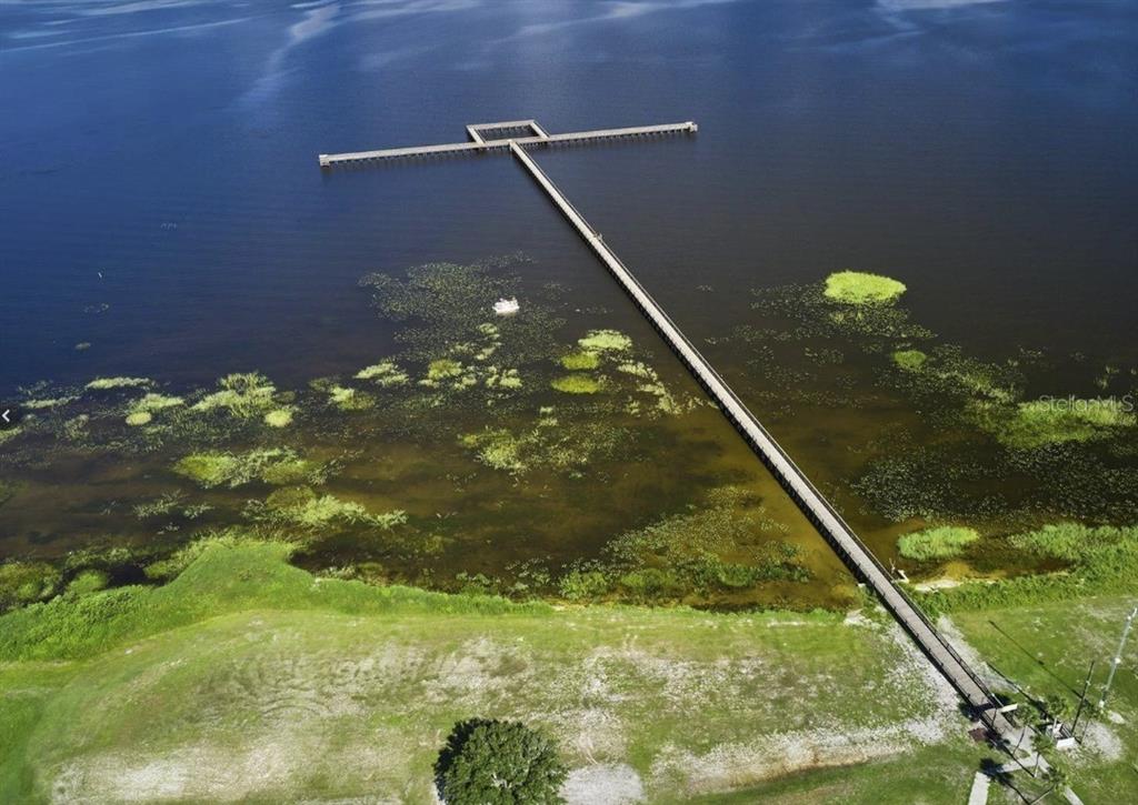 An aerial view shows a long wooden pier extending from a grassy shore into a lake — 164 DESOTO AVENUE, INDIAN LAKE ESTATES, FL