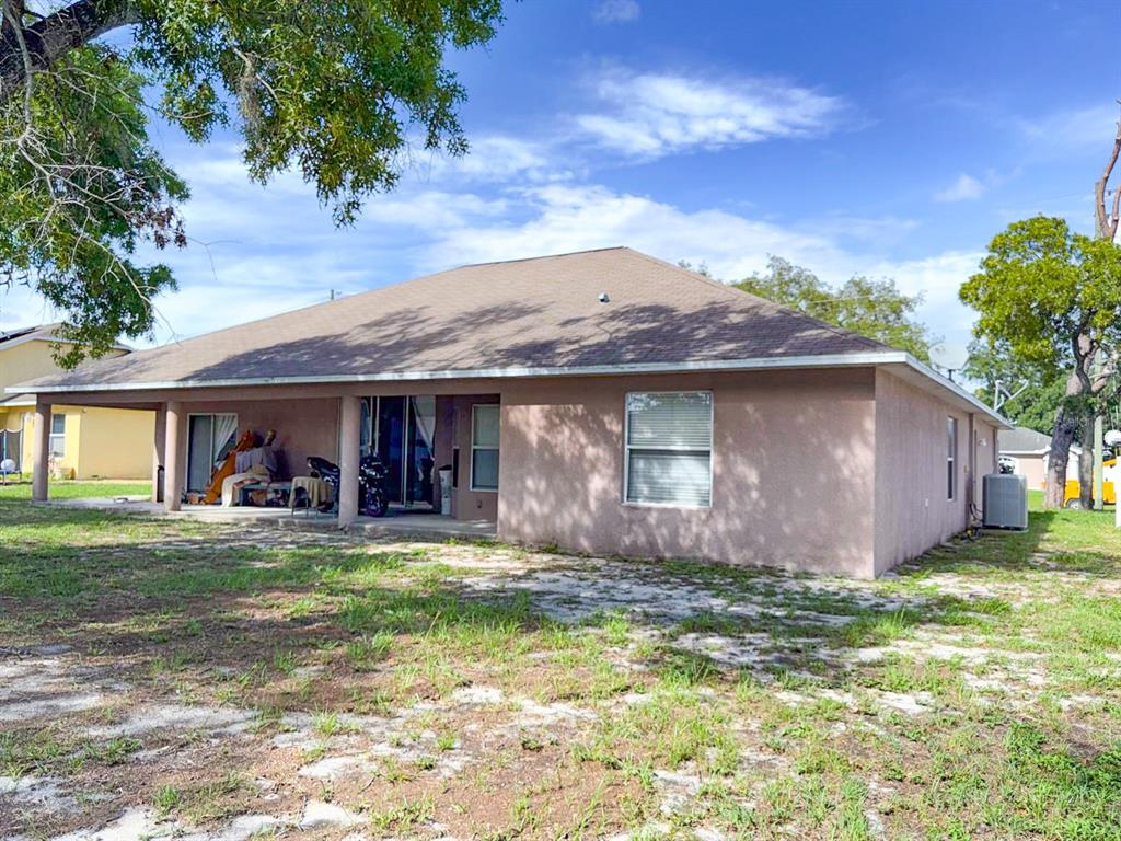 The rear exterior of a single-story stucco house features a covered patio and a yard — 8414 BAY DRIVE, SPRING HILL, FL