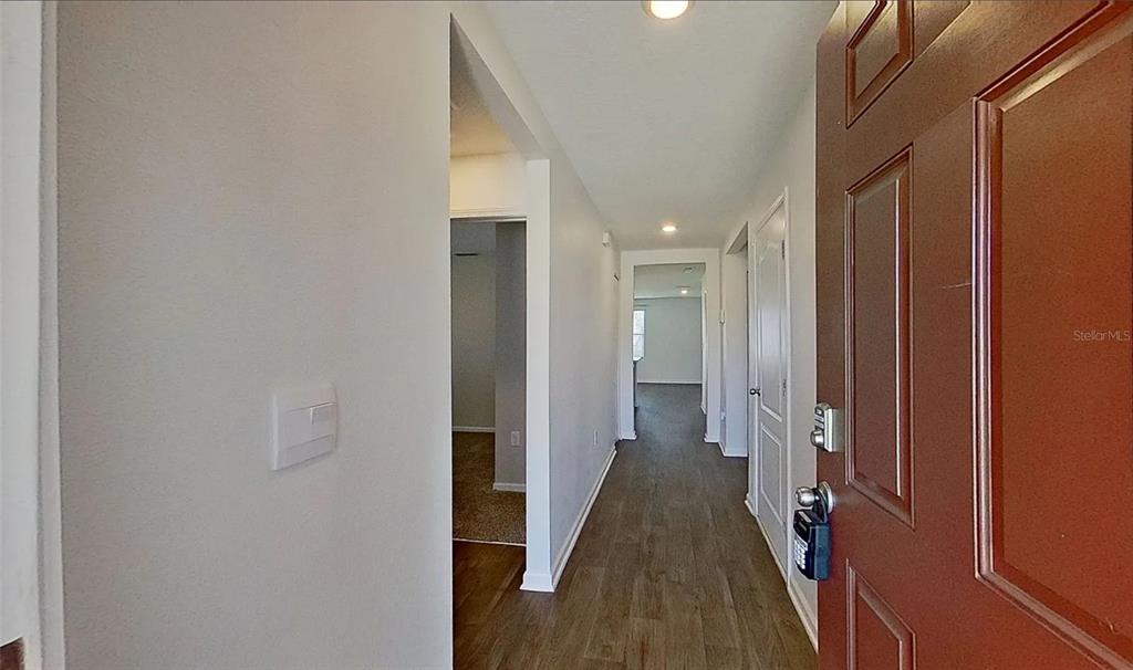 An interior view shows a hallway with wood-look flooring leading to an open living area — 5471 HOLLOW BIRCH DRIVE, JACKSONVILLE, FL