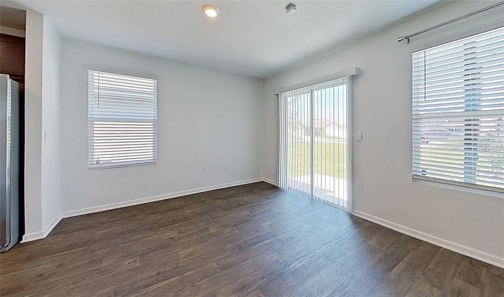 An empty room with wood-look flooring, two windows with blinds, and a sliding glass door — 5471 HOLLOW BIRCH DRIVE, JACKSONVILLE, FL