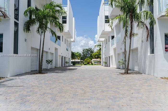 A paved driveway sits between two modern, white multi-story residential buildings with palm trees — 1985 Calais # 3, Miami Beach FL 33141, MIAMI BEACH, FL
