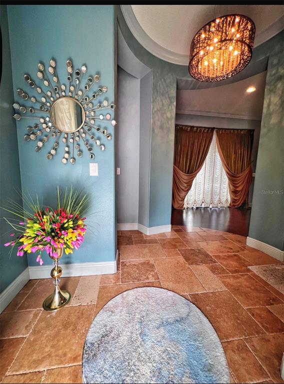 An entryway features a sunburst mirror, a floral arrangement, and a chandelier over tiled floors — 9406 DUGARD COURT, ORLANDO, FL